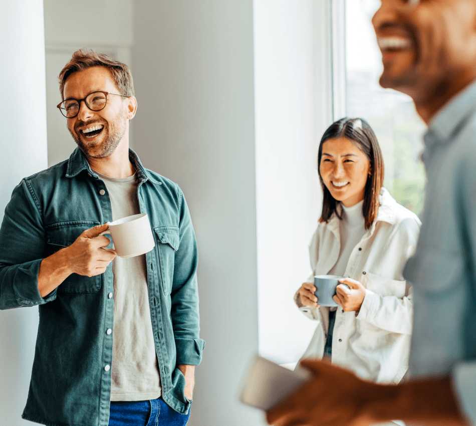 A happy group of small business employees drink coffee and laugh together.